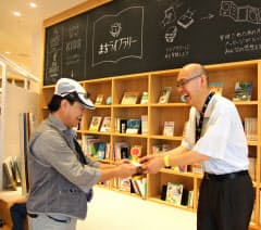 「おおさか歩き案内人」の名刺を渡す奥村武資さん(右、大阪市中央区のまちライブラリー）